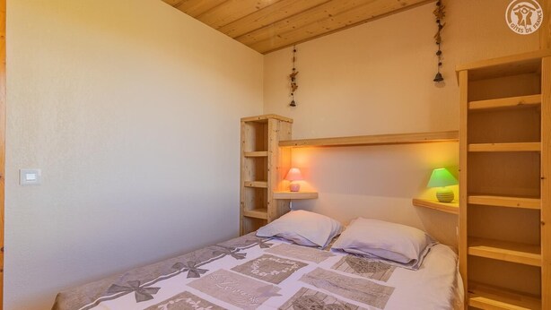 Un dormitorio con una cama, dos lámparas de noche, una estantería de madera y un aplique de pared.