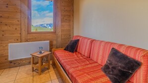 A cozy room with a wooden interior, a red patterned sofa, two dark cushions, a small wooden table with a glass, and a window with a view of a green landscape. - O'mikely - LE Dingo - Albiez Montrond (ALBIEZ MONTROND)