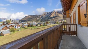 Un balcón de madera con vistas a un pueblo, casas y montañas al fondo.