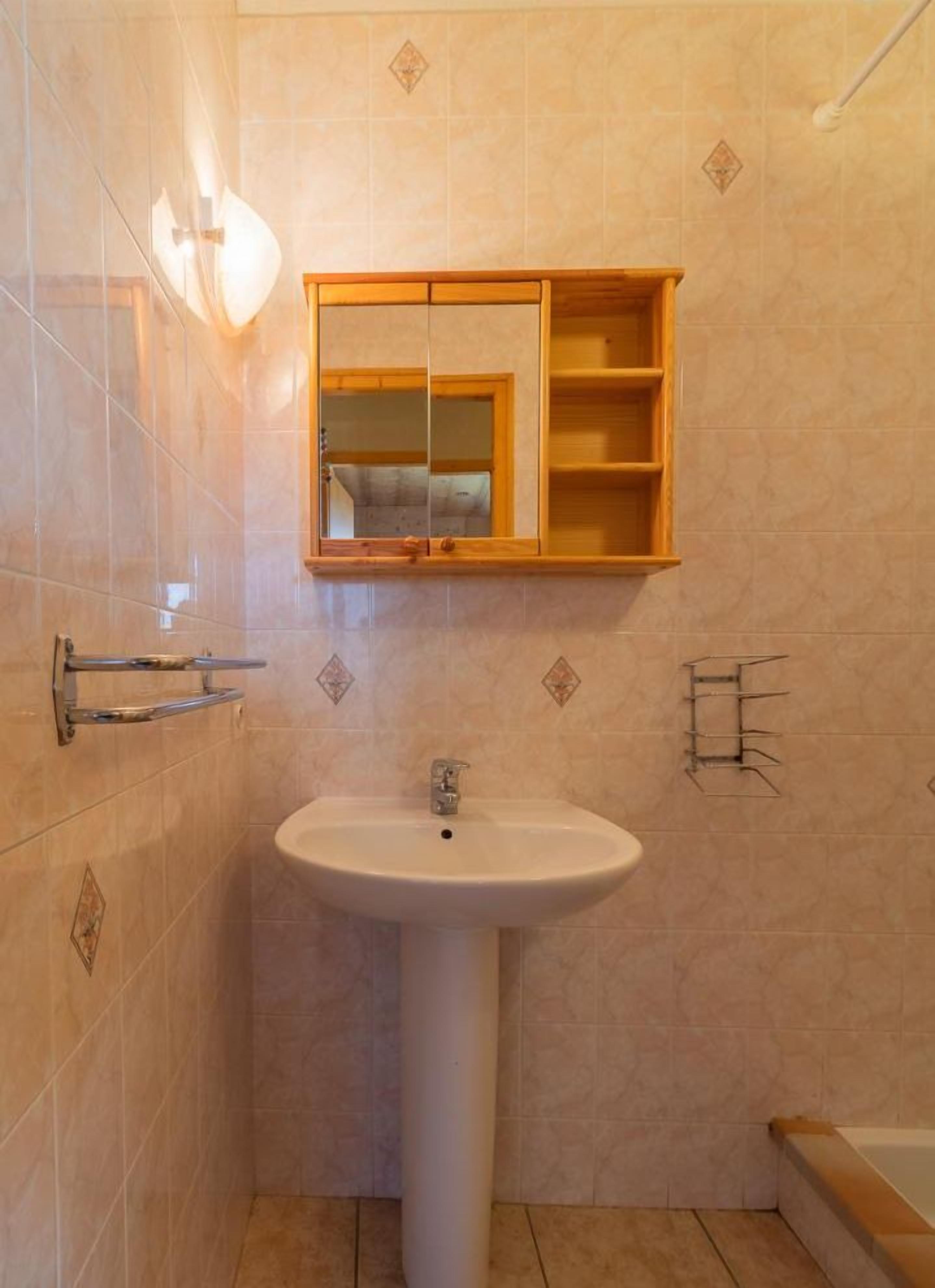 Un baño con lavamanos pedestal, tocador de madera y barra para toallas.