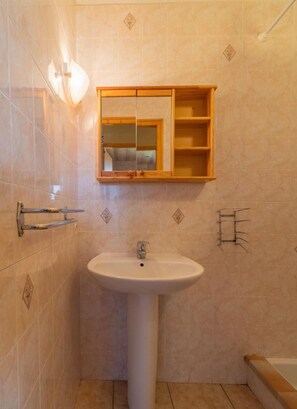 Une salle de bain avec un lavabo sur colonne, un meuble à pharmacie en bois et un porte-serviettes.