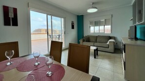 A modern living room with a sofa and a dining area with a table set for two. - ACV - Torremar-2ª Linea Planta 7 Frontal 2 (OROPESA)