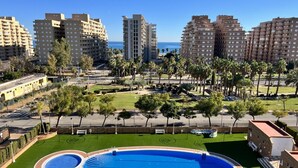 A residential area with a large circular swimming pool surrounded by green lawns and palm trees. - ACV - Torremar-2ª Linea Planta 7 Frontal 2 (OROPESA)