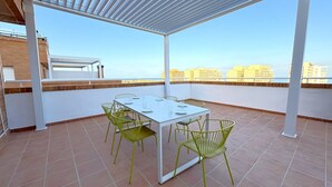 A rooftop terrace with a white table and green chairs, overlooking a cityscape. - ACV - Torremar-2ª Linea Planta 7 Frontal 2 (OROPESA)