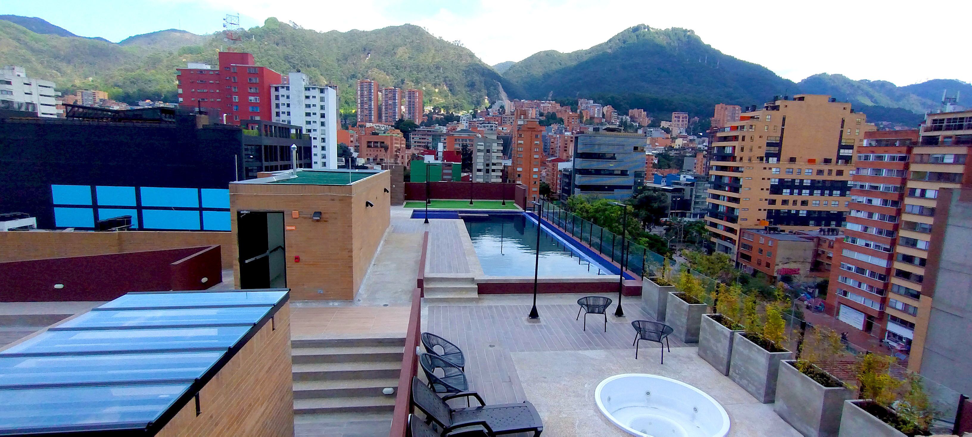 A rooftop terrace with a swimming pool, outdoor seating, and a view of a cityscape with mountains in the background.