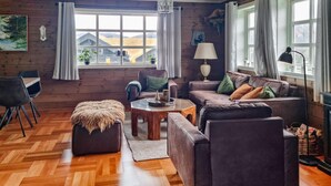 A cozy living room with a wooden floor, a sofa set, a coffee table, and a view of the outdoors through large windows. - 7 bedroom awesome home in Tjørhom (Tjørhom)