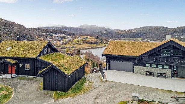 A rural area with traditional black wooden houses with grass roofs, a river in the background, and a mountainous landscape. - 7 bedroom awesome home in Tjørhom (Tj ørhom)