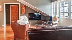 A cozy living room with a brown leather sofa, a white fluffy throw, a wooden door, a wall-mounted clock, and a large window with multiple panes. - 7 bedroom awesome home in Tjørhom (Tjørhom)