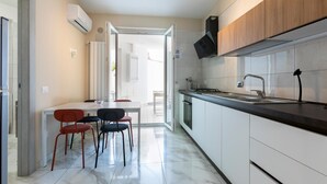 Une cuisine moderne avec des meubles blancs, un évier en acier inoxydable et un robinet noir. On y trouve également un coin repas avec une table blanche et des chaises rouges.