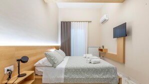 Une chambre d’hôtel moderne, équipée d’un lit, d’un bureau avec une lampe, d’un téléviseur fixé au mur et d’une fenêtre avec des rideaux.