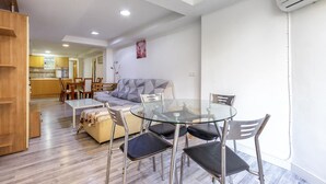 A modern living room with a glass dining table, metal chairs, a sofa, and a kitchen in the background. - 2 bedroom beautiful apartment in Benidorm (Benidorm)