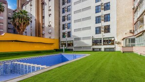 A hotel courtyard with a swimming pool, green lawn, and a yellow wall. - 2 bedroom beautiful apartment in Benidorm (Benidorm)