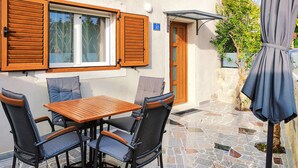 Un patio con una mesa de madera y cuatro sillas, una puerta y un cartel con número de habitación.