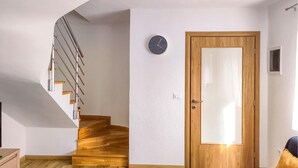 Una escalera con escalones de madera y barandillas metálicas, una puerta de madera con un panel de vidrio y un reloj fijado a la pared.