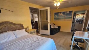 A hotel room with a bed, a desk, a chair, a ceiling fan, and a door leading to a bathroom. - Beach House with Pool (Englewood)