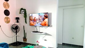 Ein Wohnzimmer mit Fernseher, einem Kaktus, einem Ventilator und einem blauen Sofa.