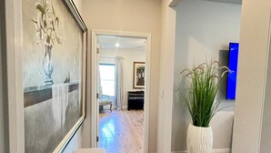 Un pasillo con un banco, una obra de arte enmarcada, una planta en maceta y un objeto azul en la pared.