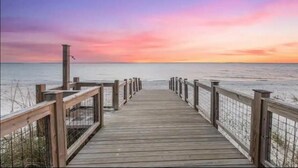 Un paseo marítimo de madera que conduce a la playa, con un atardecer de fondo.