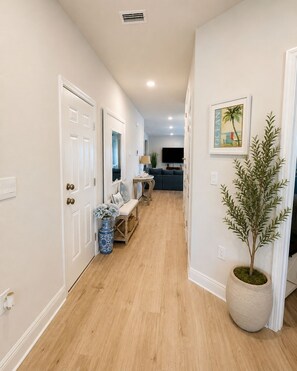 Un couloir avec un plancher en bois, un coin salon avec un canapé et des fauteuils, une plante en pot et un tableau accroché au mur.