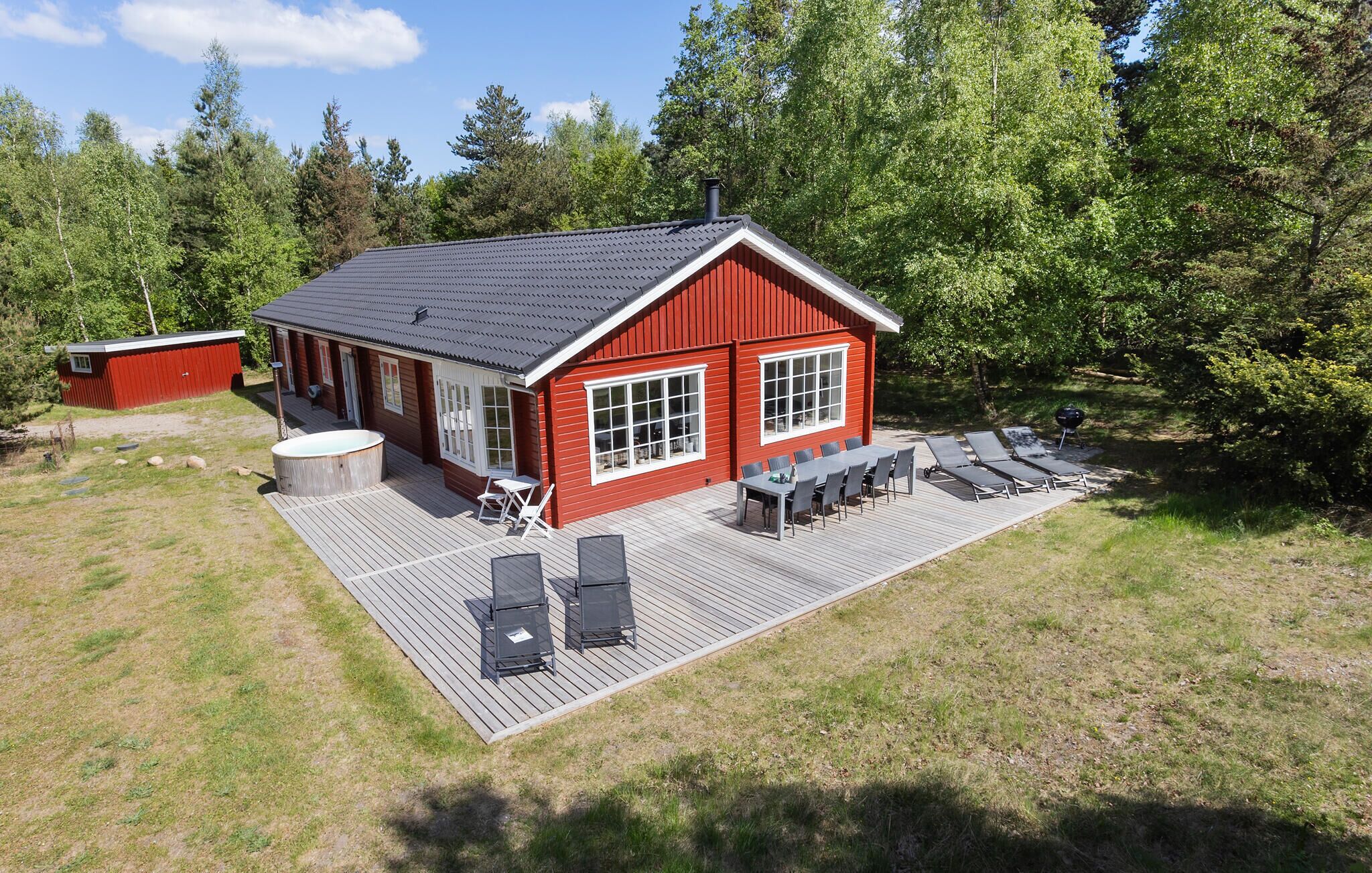 A red wooden cabin with a deck, a hot tub, and a barbecue area.