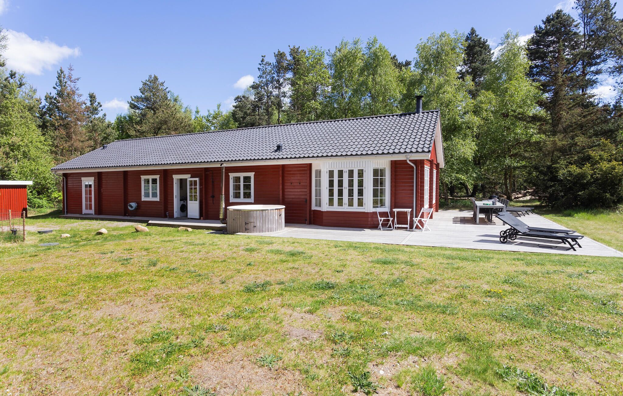 A red wooden house with a tiled roof, a hot tub, and a patio with outdoor furniture.