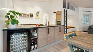 A modern kitchen with a built-in wine cooler, a dining area with a wooden table and chairs, and a staircase leading to an upper level.