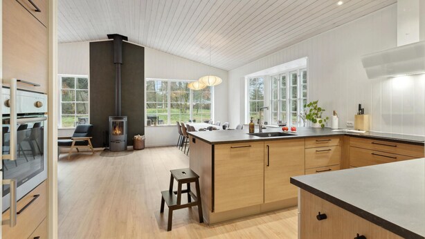 A modern kitchen with a central island, wooden cabinets, and large windows.