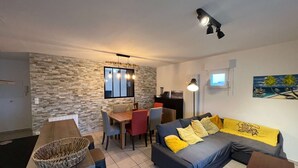 Ein modernes Wohnzimmer mit Steinwand, Essbereich mit Holztisch und -stühlen, Sofa mit gelben Kissen und Wand-Fernseher.