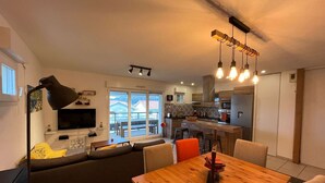 Ein modernes Wohnzimmer mit Esstisch aus Holz, einer Couch und einem Fernseher.