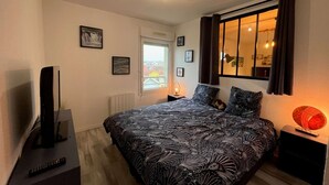 Ein Schlafzimmer mit einem Bett, einem Fernseher, einem Fenster und einem Nachttisch mit Lampe.