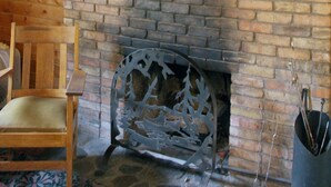 A rustic cabin interior with a mounted moose head on the wall, a brick fireplace, wooden furniture, and a decorative metal piece above the fireplace. - High Mountain 3 BR log home w/ fireplace (Lake City)