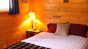 A wooden cabin room with a bed, a nightstand, a lamp, and a window with curtains. - High Mountain 3 BR log home w/ fireplace (Lake City)