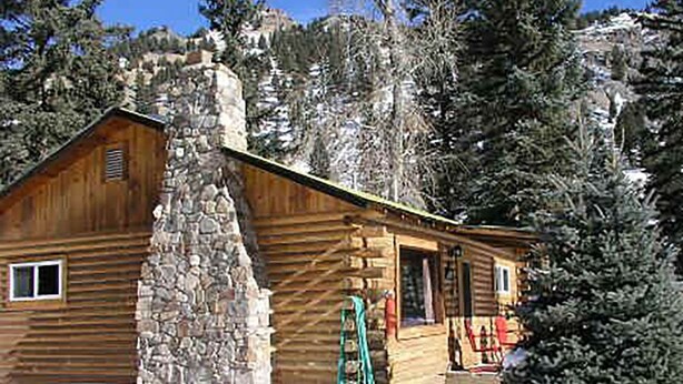 A log cabin with a stone chimney, surrounded by snow-covered trees and a clear sky. - High Mountain 3 BR log home w/ fireplace (Lake City)