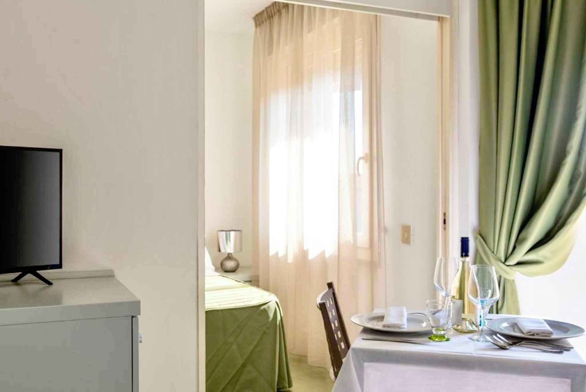 Une chambre d’hôtel avec un lit, une télévision et une table à manger dressée avec des assiettes, des verres et une bouteille.