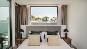 A hotel room with a large bed, two bedside tables with lamps, a window with curtains, and a view of the outside. - AVASARALA by Buenavilla | A 3 bedroom luxury villa in Puerto Calero (Puerto Calero)