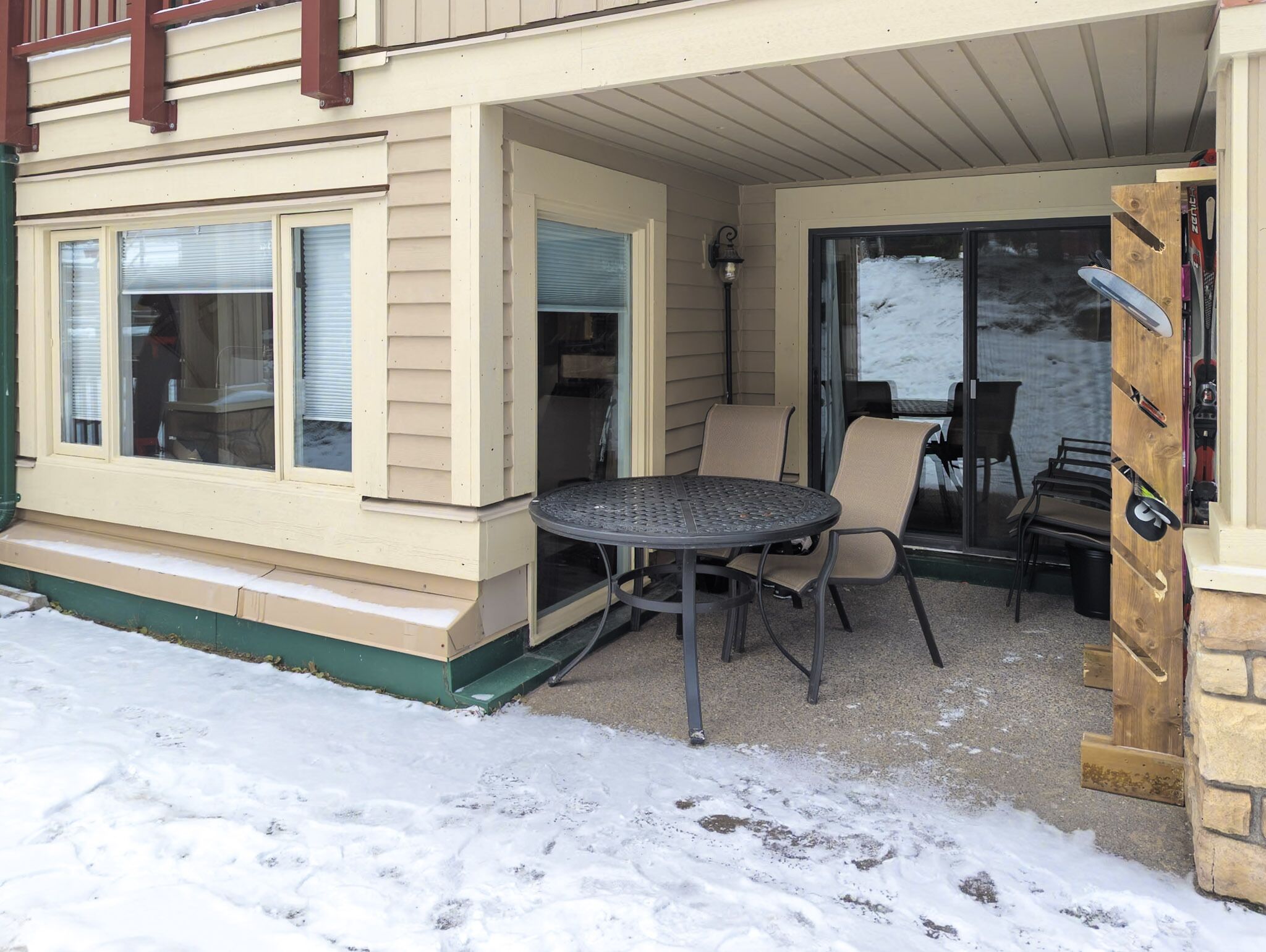 A covered patio with a table and chairs, a sliding glass door, and a wooden door with a ski rack.