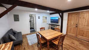 Une pièce chaleureuse avec une table à manger en bois, un canapé gris et un téléviseur fixé au mur.