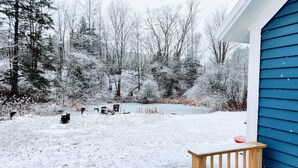 Une cour arrière enneigée avec une terrasse en bois et une maison bleue.