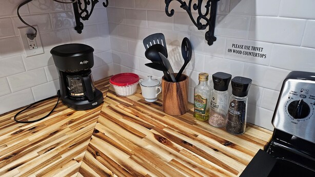 Une cuisine équipée d’une machine à café, d’une théière blanche, d’un porte-épices en bois et d’une plaque de cuisson en acier inoxydable à l’avant.