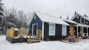 Une maison à deux étages, dont le toit est recouvert de neige et qui possède une terrasse en bois.