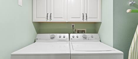A laundry room with two white washers and dryers, white cabinets above, and a green wall.
