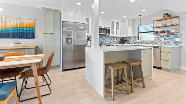 A modern kitchen with a central island, stainless steel appliances, and a dining area with a table and chairs. - Seaside Escape | Modern 2BR w/ Balcony, Pool & Ocean Views!🌴 (Cape Canaveral)