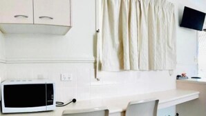 Uma cozinha com micro-ondas, duas cadeiras e uma cortina.