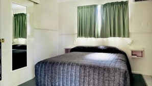 Quarto com uma cama de solteiro, mesa de cabeceira, janela com cortinas verdes e um espelho na parede.