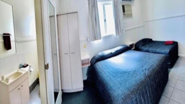 Quarto com cama, escrivaninha, guarda-roupa e janela.