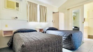 Quarto de hotel com duas camas, um guarda-roupa, um espelho e uma janela com cortinas.