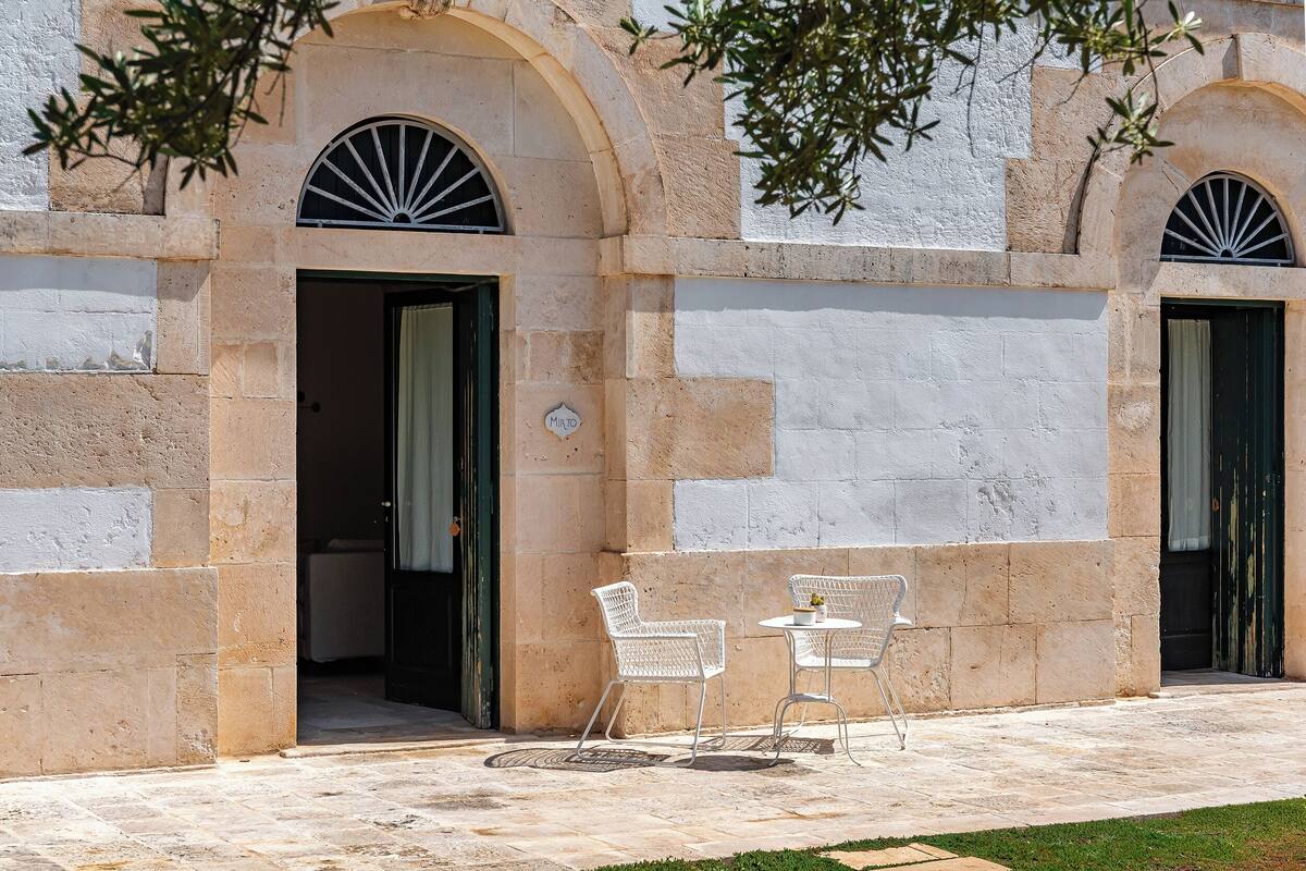 Un bâtiment doté de portes en arc de cercle, un petit espace extérieur aménagé avec deux chaises et une table, et une enseigne indiquant le nom « Mundo ».