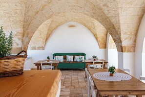 A room with a stone vaulted ceiling, a green sofa with white cushions, a wooden table, and a woven basket. - masseria gorgognolo (Ostuni)