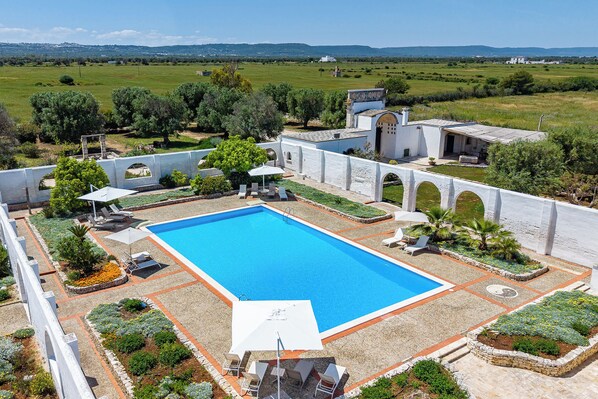 Una piscina con cubierta blanca, rodeada por un muro blanco con arcos, y vistas a un paisaje verde.