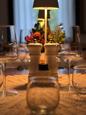 Una mesa lista para comer, con saleros y pimenteros, una vela y un florero con flores.